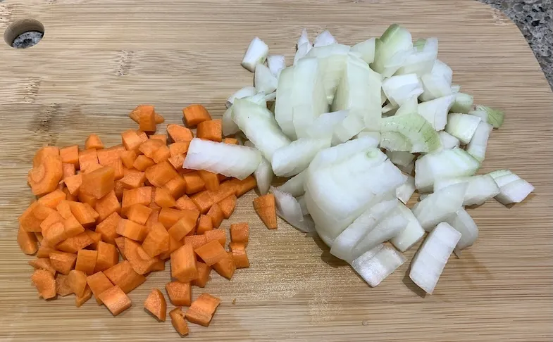 Diced carrot and onion on a wooden chopping board