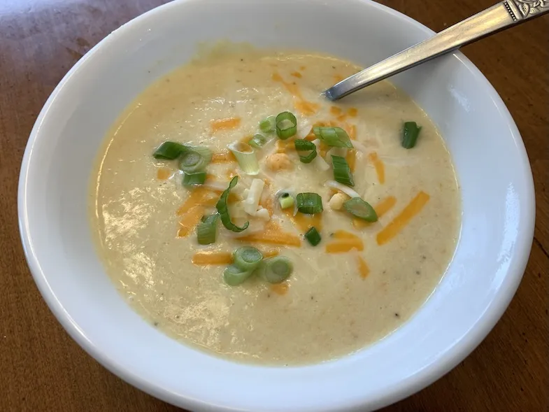 Bowl of gluten-free cauliflower soup with cheese and green onion garnish